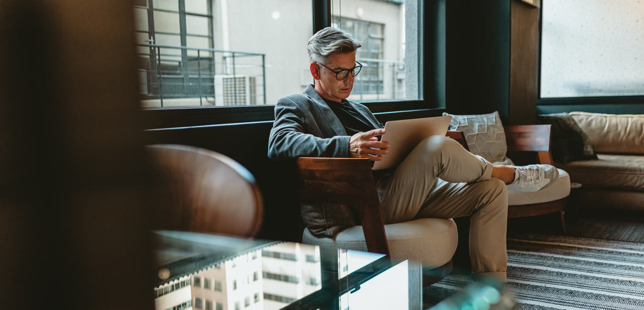 A man is sitting on a chair in a co-working space and looking on his laptop screen